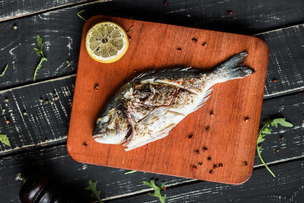 whole grilled fish on wooden board with sliced lemon