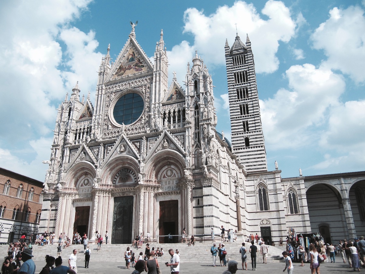 White Gothic cathedral in an Italian piazza on a mostly sunny day