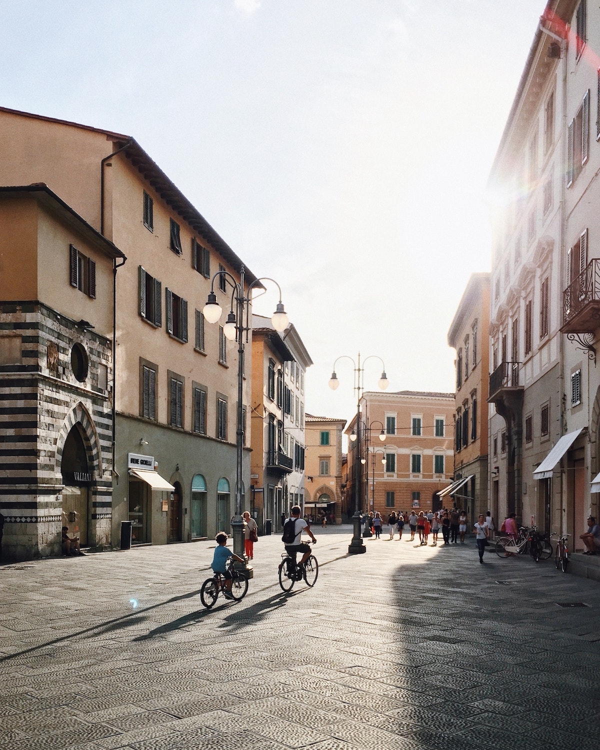 Children riding bikes in a wide pedestrian street in Italy on a sunny day