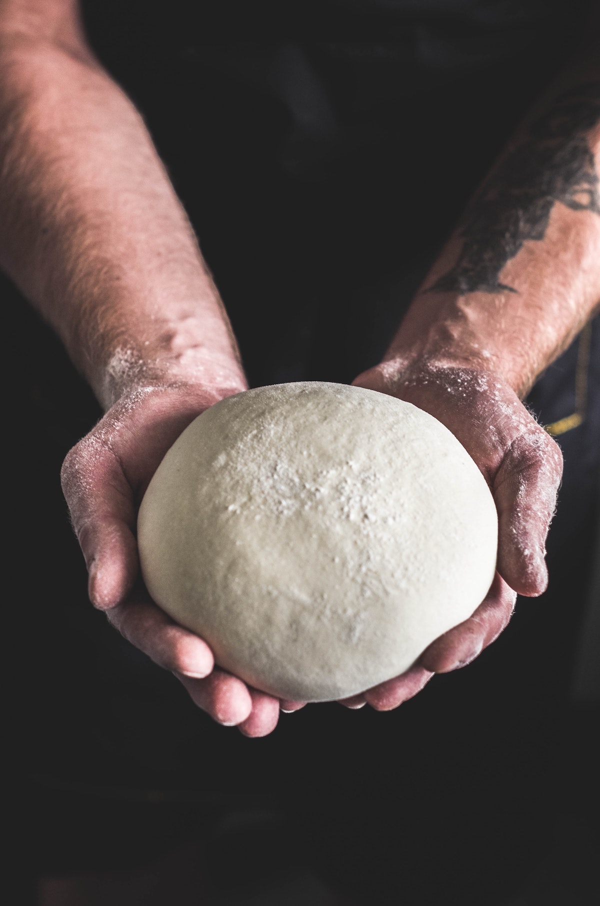 Person's hands holding a ball of pizza dough.