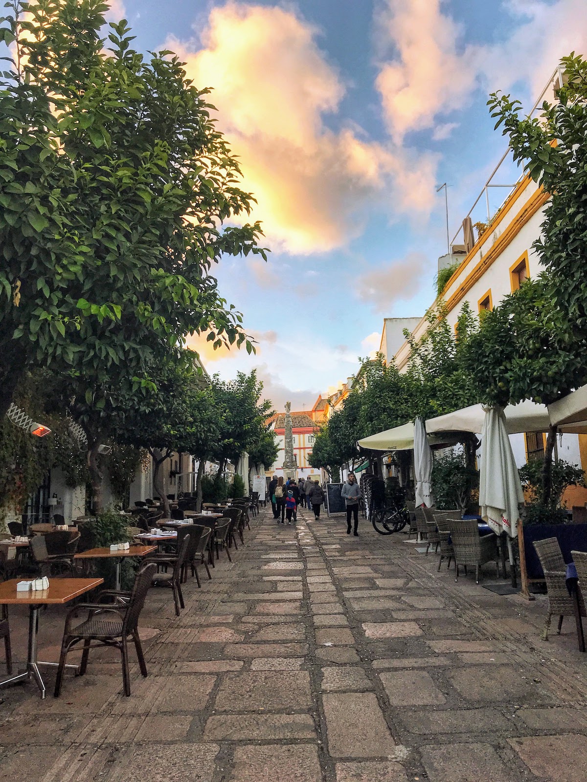 Cobblestoned plaza at sunset lined with restaurant tables on either side.