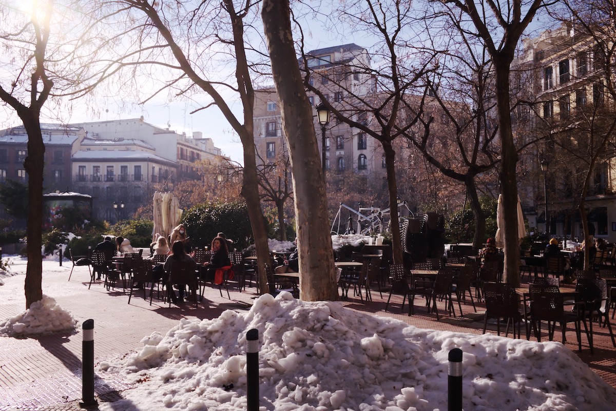 Sunny hidden plaza in Madrid with terrace seating and some piles of snow.