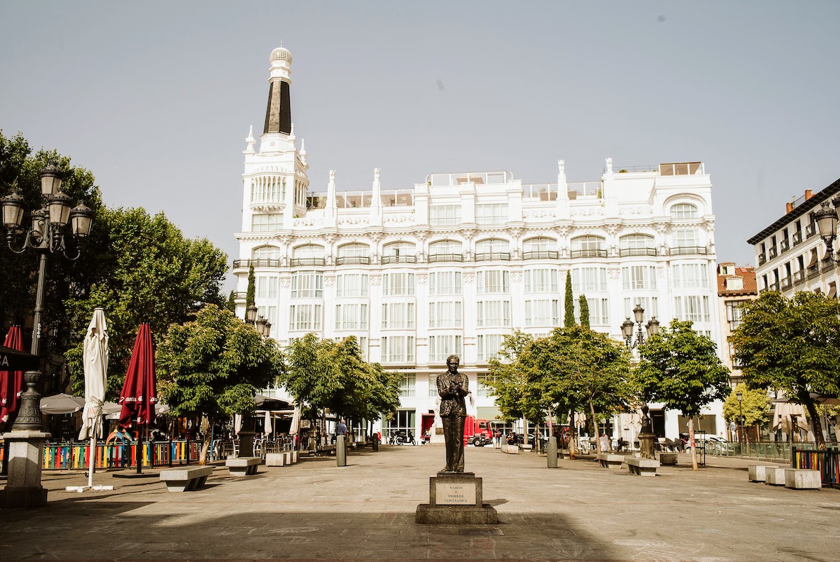 Urban plaza with a statue of a man in the foreground and a large white hotel in the background.