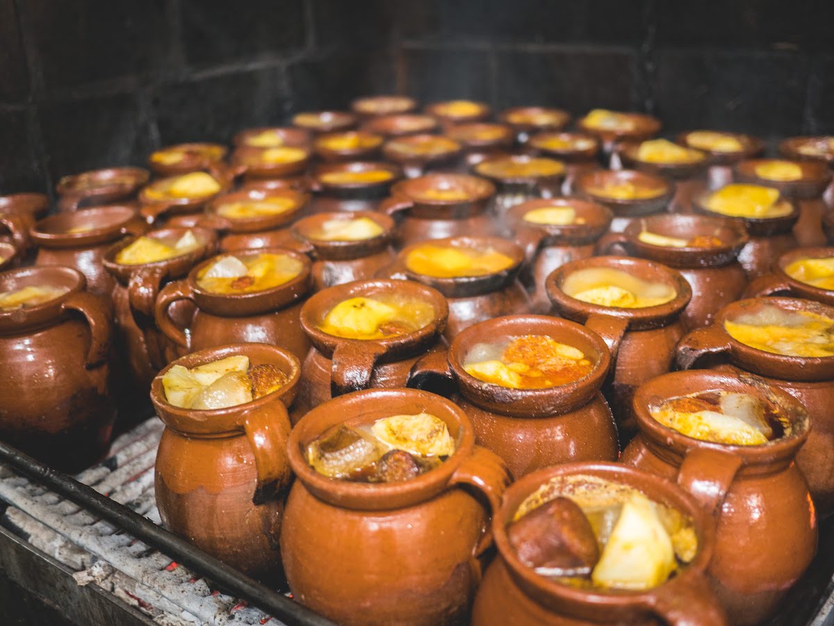 Dozens of terra cotta jars filled with a meat stew simmering on a charcoal stove