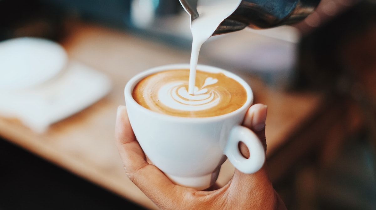 Close up of barista pouring milk into a cup of coffee