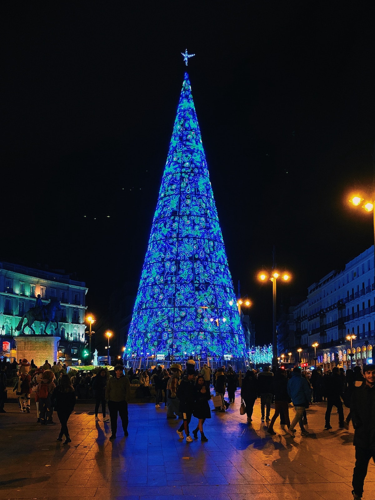 Large blue Christmas tree in a city plaza at night