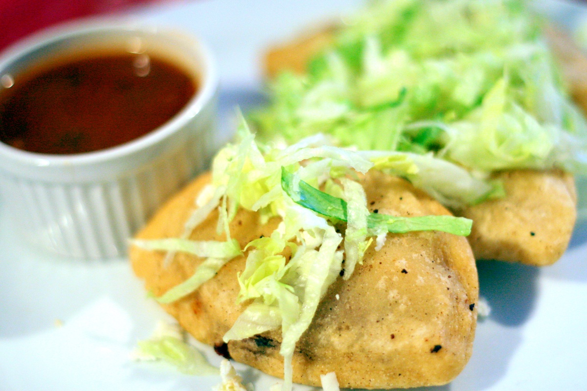 Two corn pupusas topped with shredded lettuce, with a small dish of dark red sauce on the side.