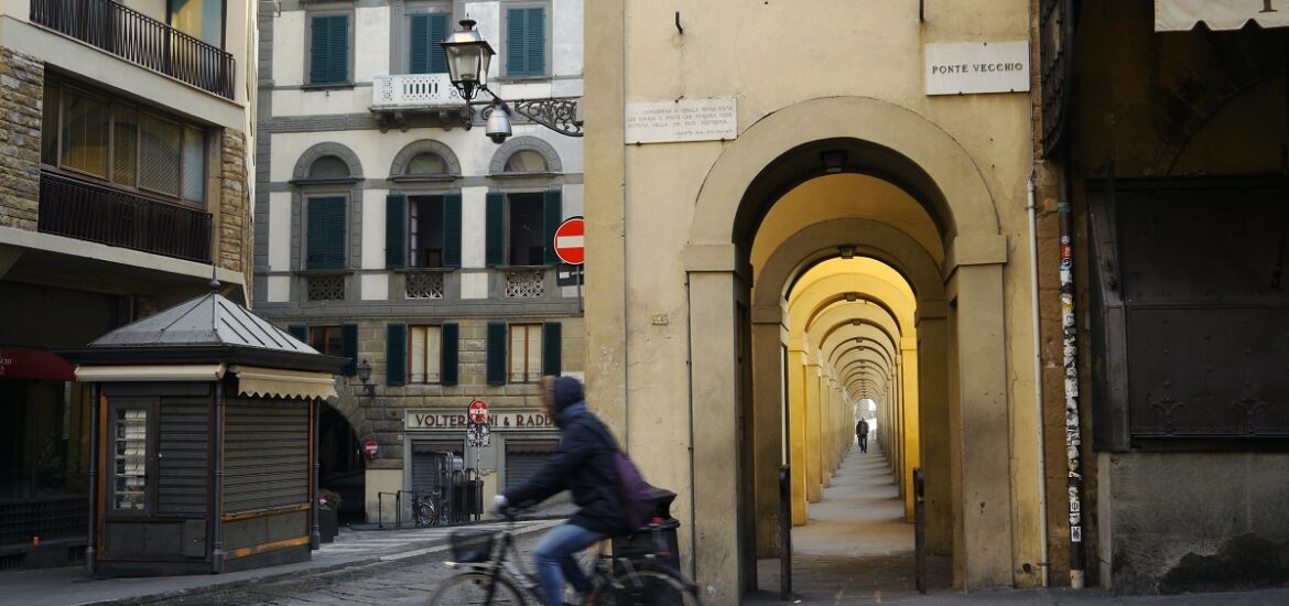 A man rides his bike by the Ponte Vecchio in the early morning in Florence