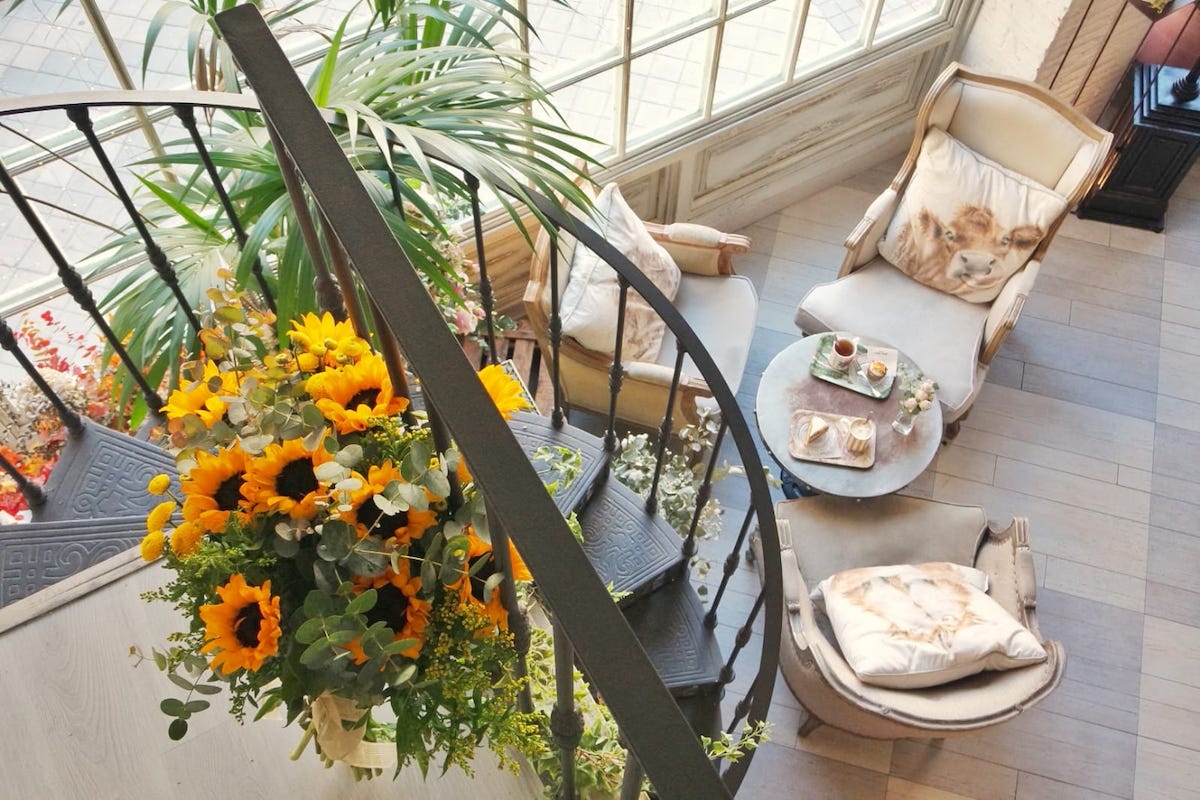 View from above of a spiral staircase decorated with sunflowers leading down into an elegant tea room.