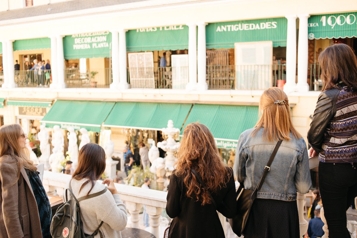 Group of people from behind facing storefronts with green awnings discovering hidden gems in Madrid.