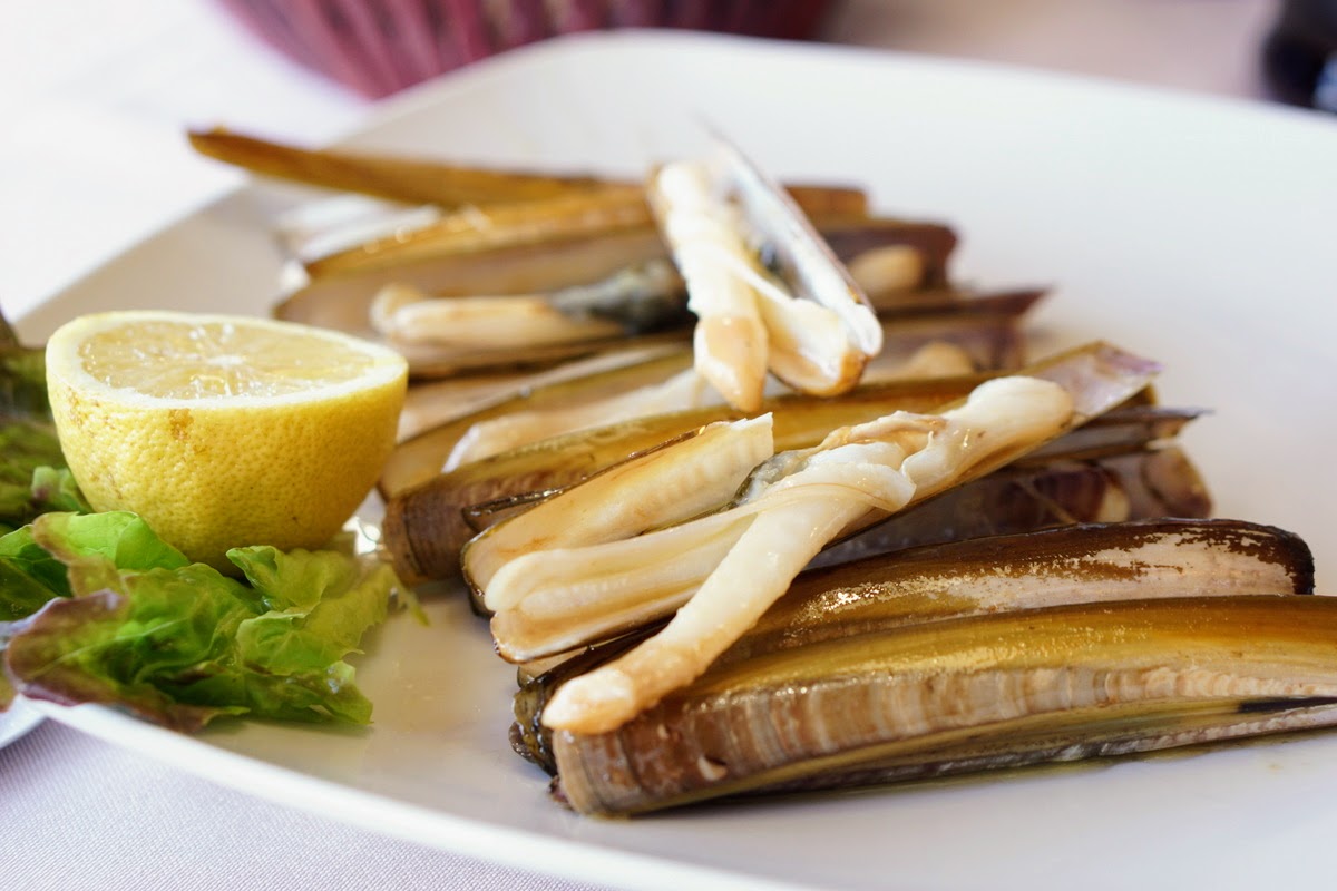 Razor clams and half of a lemon on a white plate.
