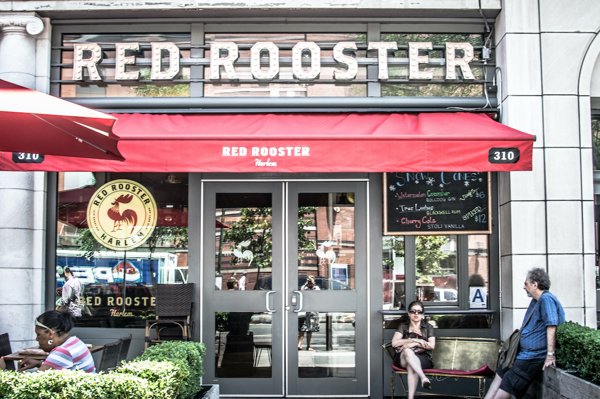 Exterior of Red Rooster restaurant in Harlem, NYC with a red awning above the doorway