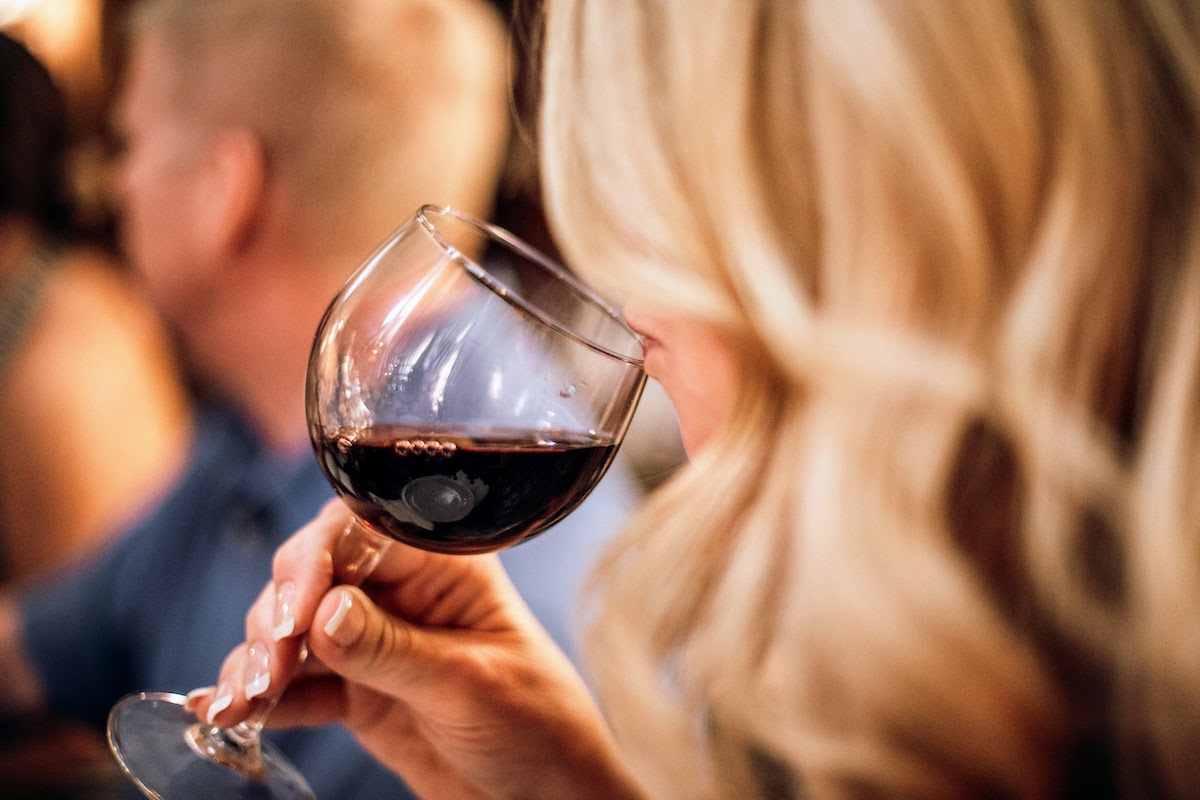 A blond woman smelling a glass of red wine