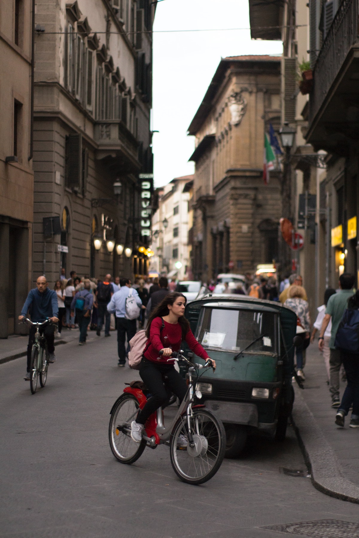Woman in a red shirt riding a bike on a busy city street