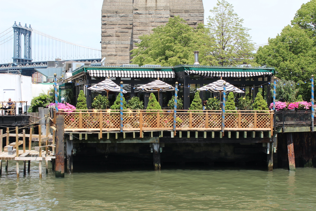Small romantic restaurant in NYC with flowers and umbrellas on the patio situated on a dock above a body of water