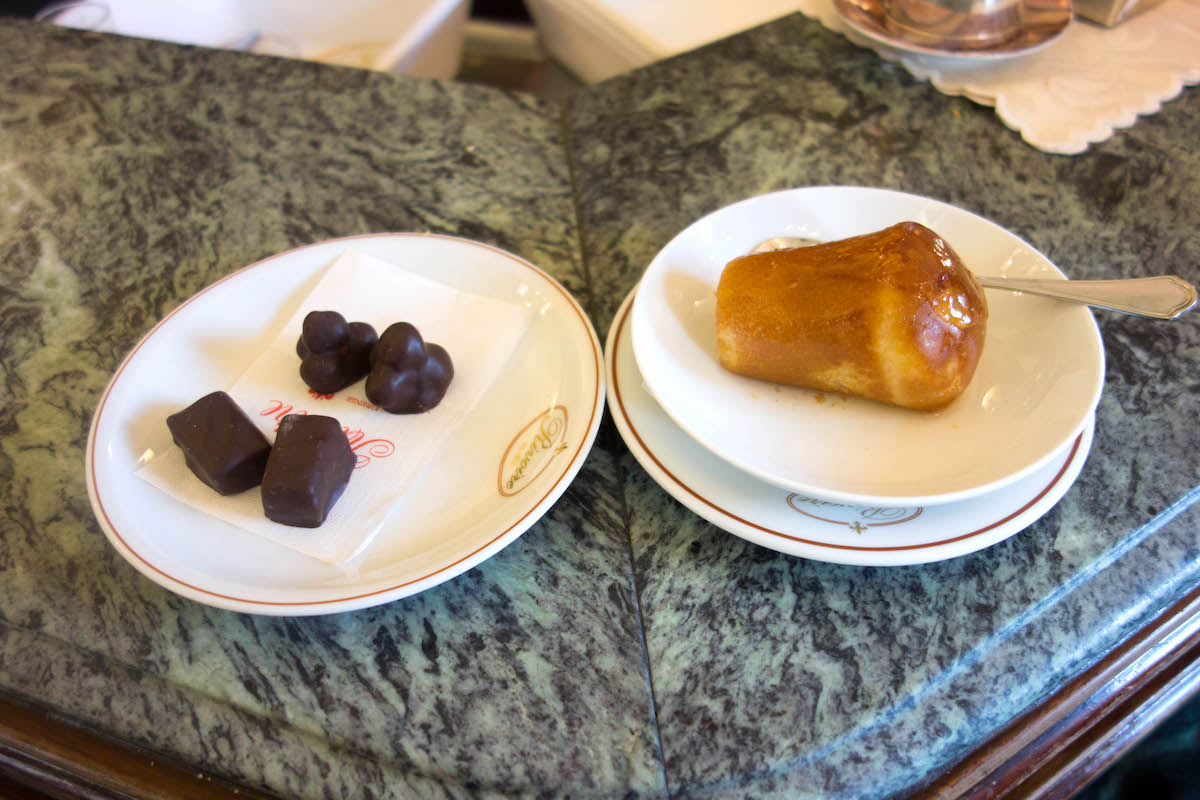 Plate of four small chocolates next to a rum baba pastry on a separate plate.