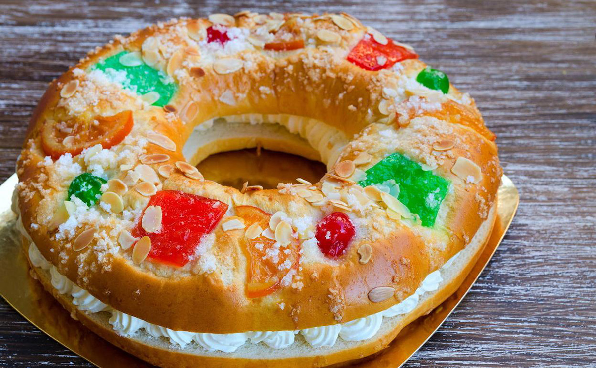 Large donut-shaped cake filled with whipped cream and decorated with red and green candied fruit.