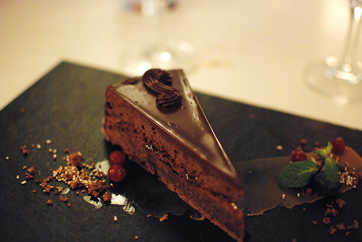 Piece of chocolate cake served on a small black tray garnished with small red berries.