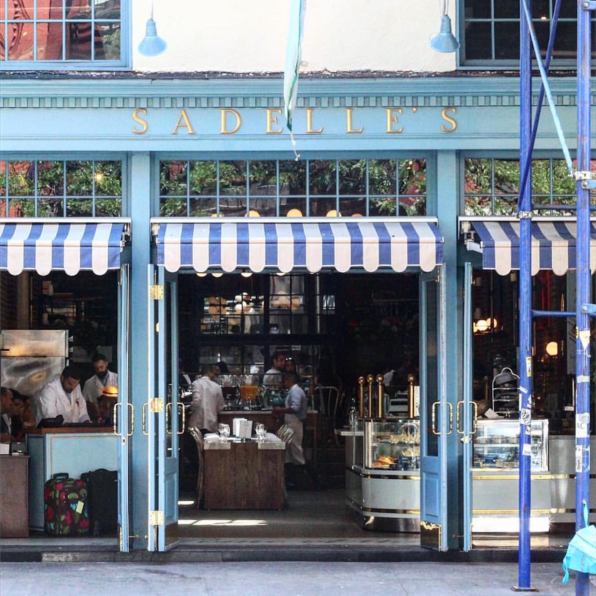 Exterior of Sadelle's in SoHo, New York, with blue paneling and a blue and white striped awning