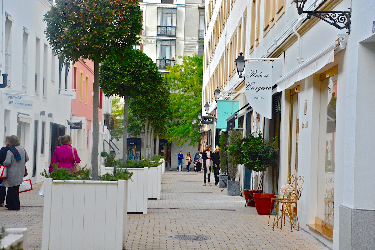 Pedestrian street decorated with plants and lined with small boutique shops.