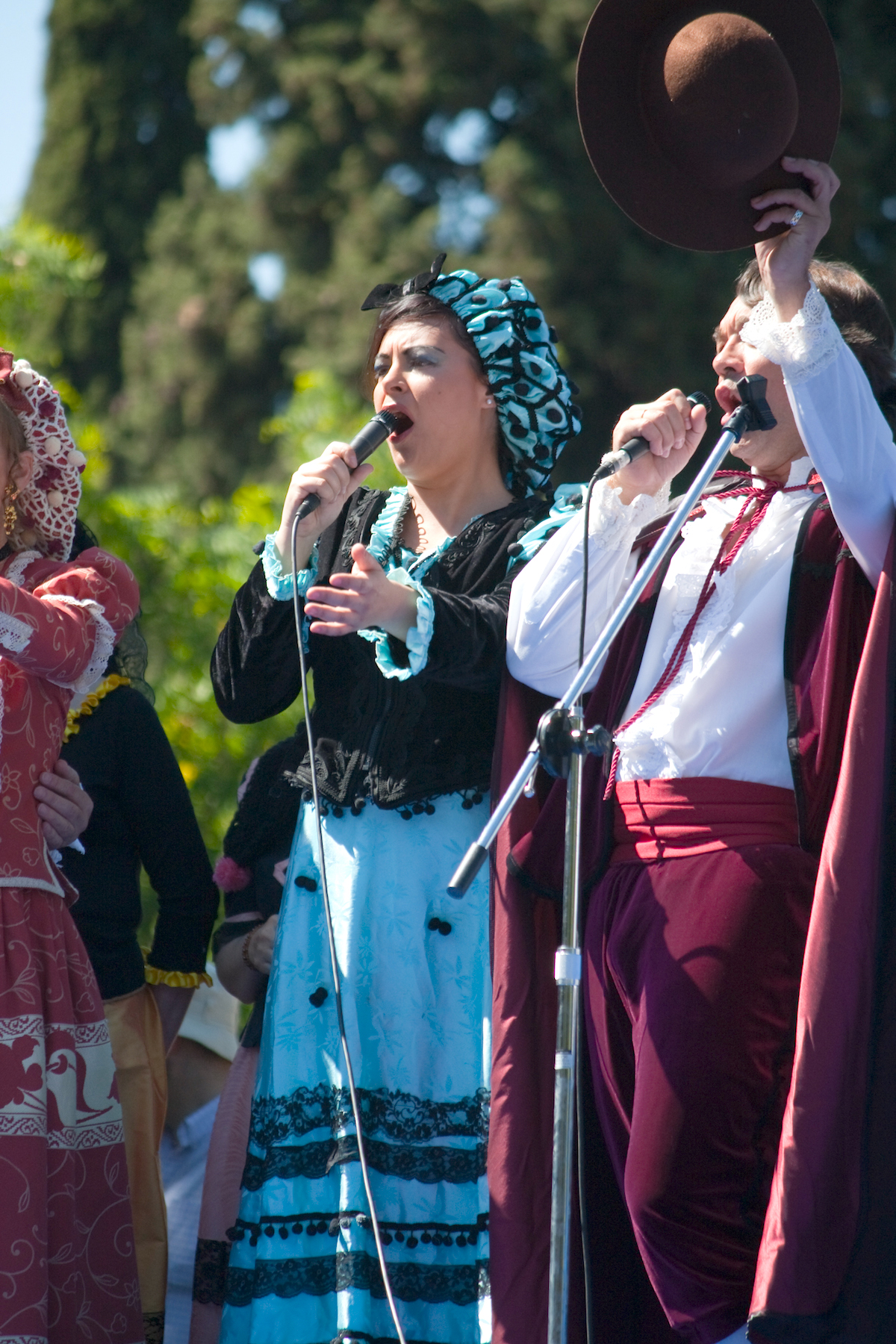 Women and men in traditional costumes holding microphones while performing at the San Isidro Festival in Madrid.