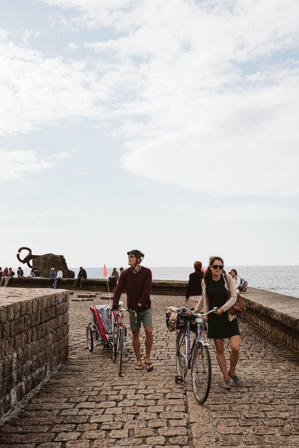 People walking their bikes on a stone seaside path.