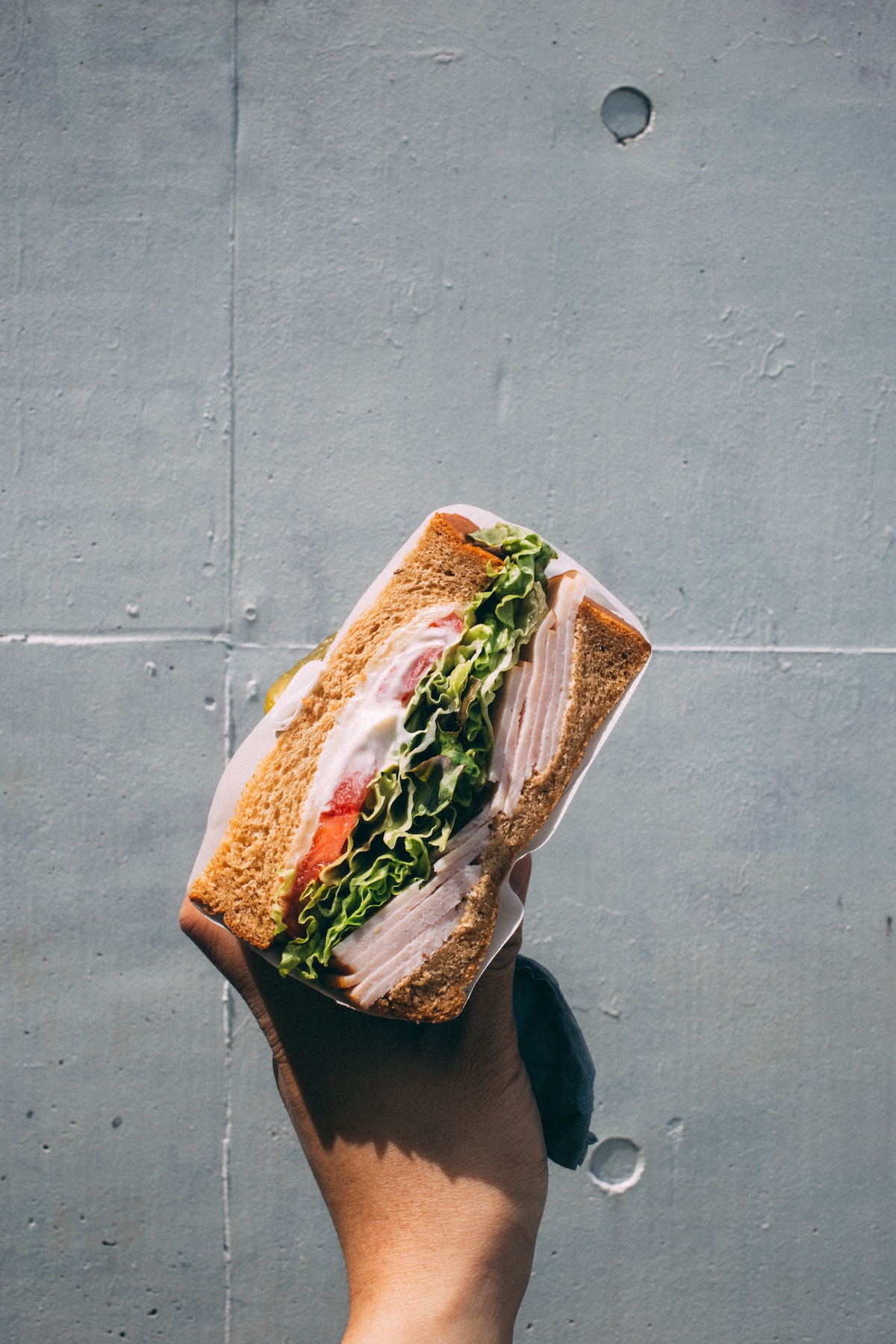 Person's hand holding a sandwich filled with meat and leafy greens