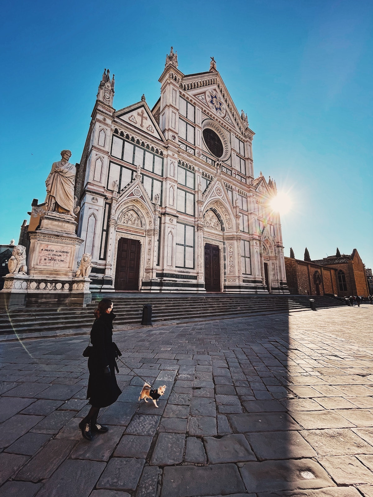 Woman walking her dog in front of a large church in Florence, Italy on a clear day.
