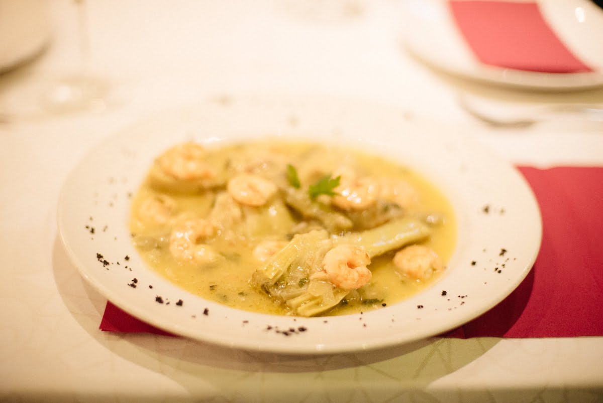 Shrimp and vegetables in a light yellow sauce on a white plate.