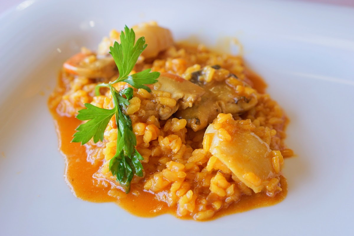 Seafood rice in a brownish-orange broth garnished with fresh herbs.