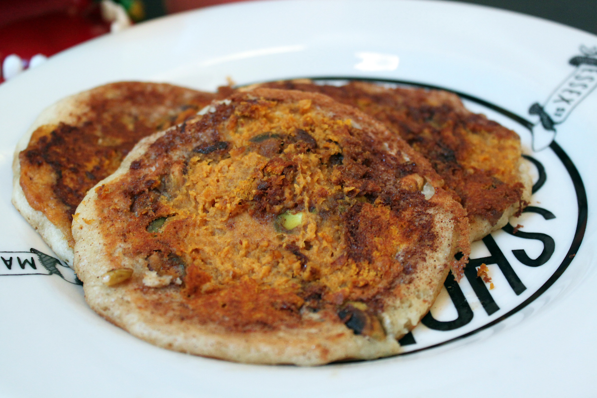 Three pancakes with glazed pumpkin, peanut butter, and pistachio on a white plate