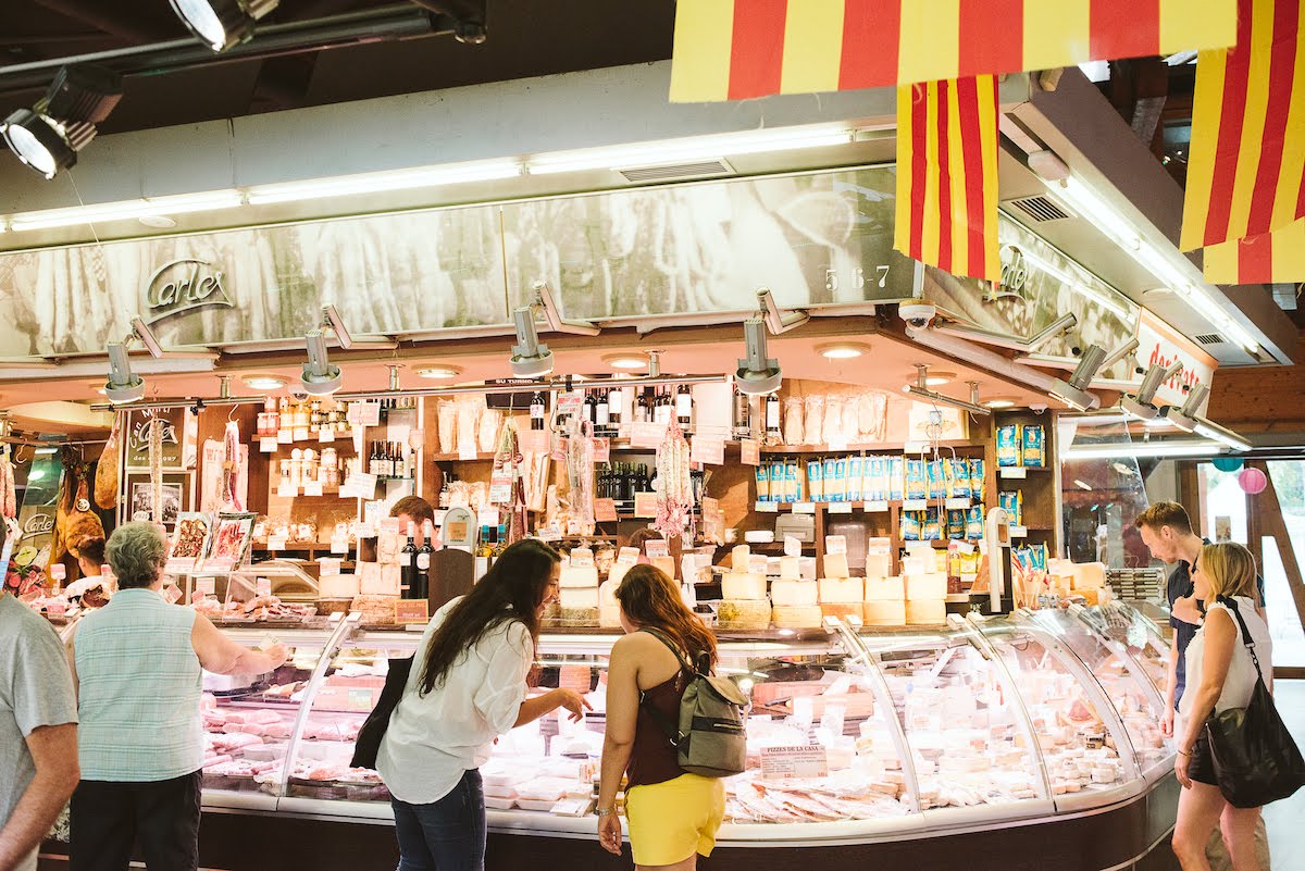 Two women shopping at a cheese stall inside a Spanish food market