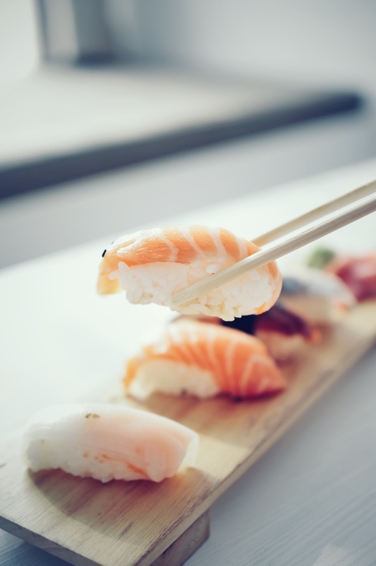 A shrimp sushi roll being held above a small sushi plate with chopsticks