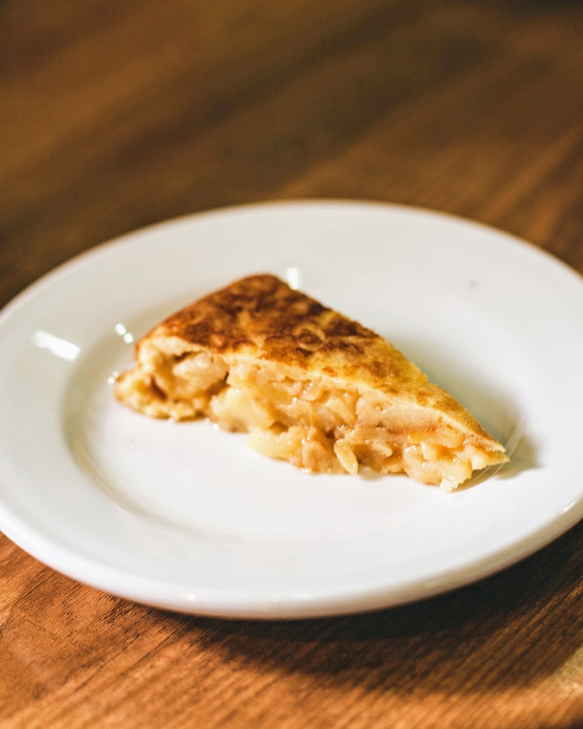 A slice of Spanish potato omelet on a round white plate at a restaurant in Madrid