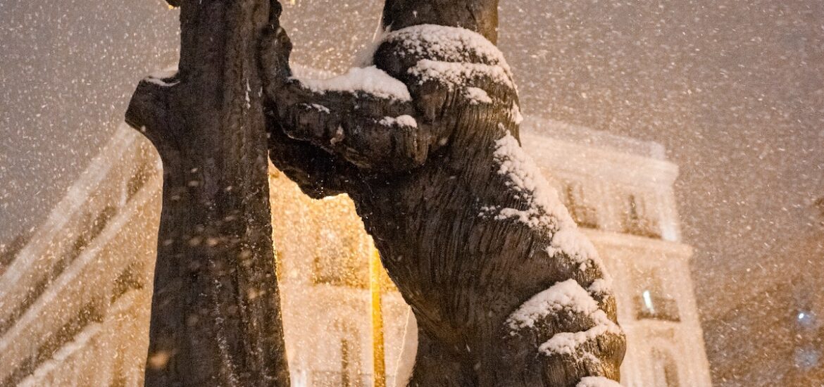 A statue of a bear eating from a tree, partially covered in snow.