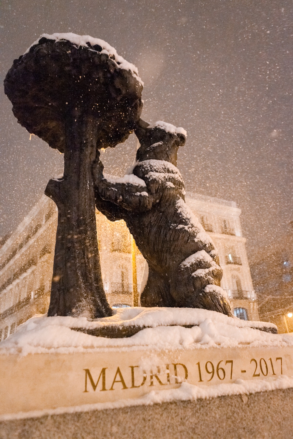 A statue of a bear eating from a tree, partially covered in snow.