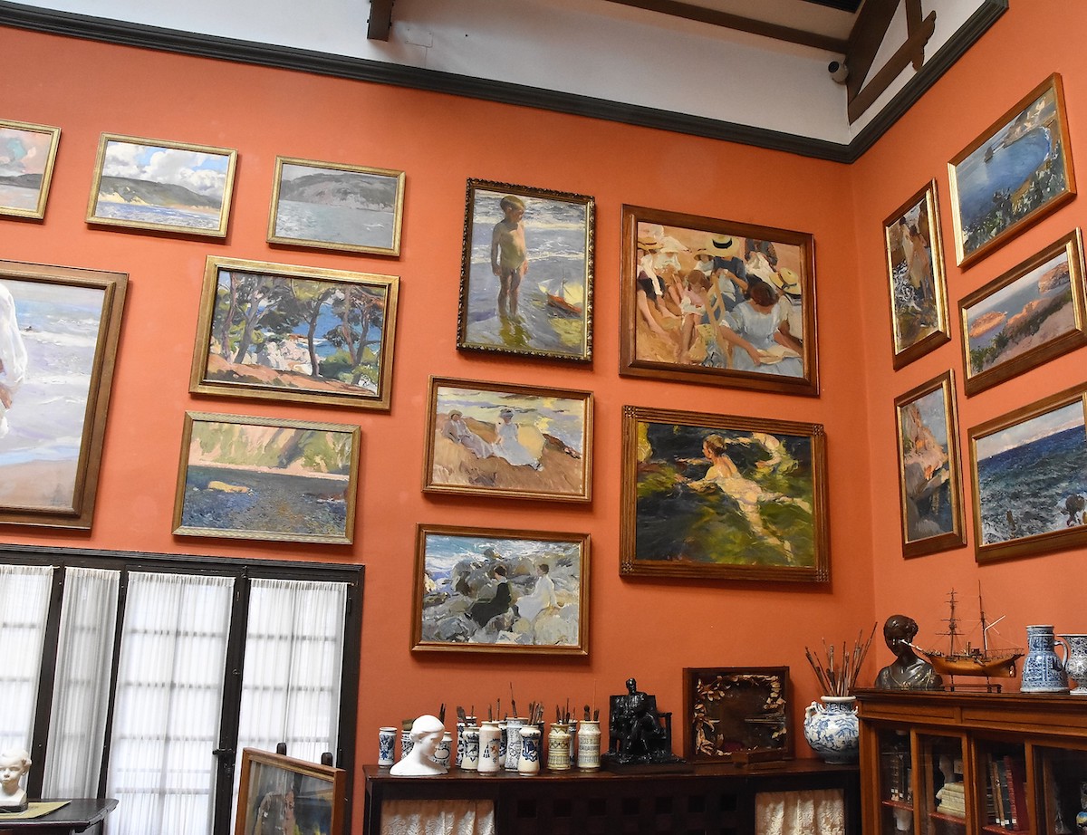 Room with orange walls covered in paintings.