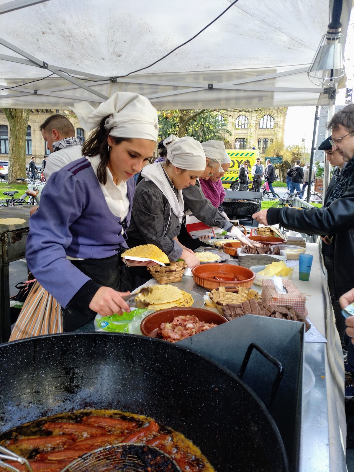 Women in traditional Basque dress serve food from a market stall