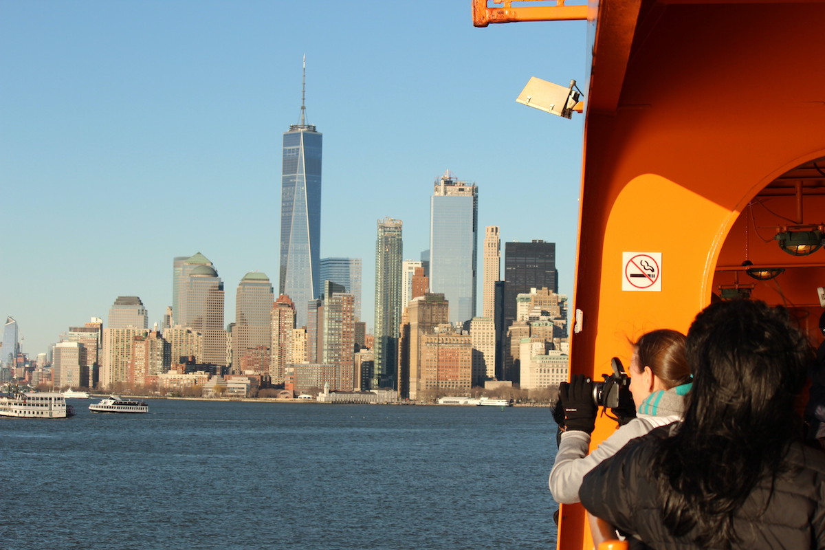 View of people on an orange ferry taking photos of the Manhattan skyline.