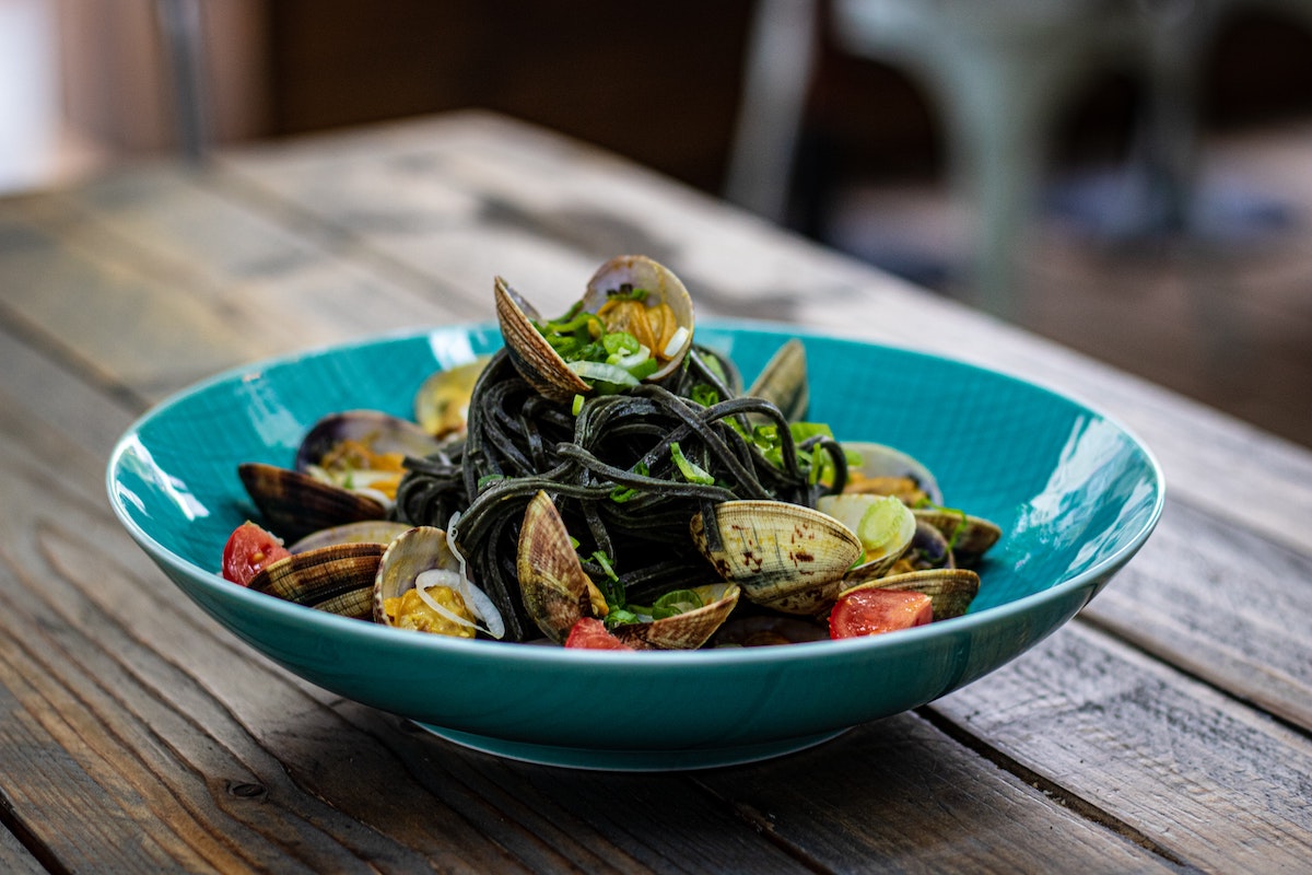 A blue bowl with black squid ink spaghetti topped with clams