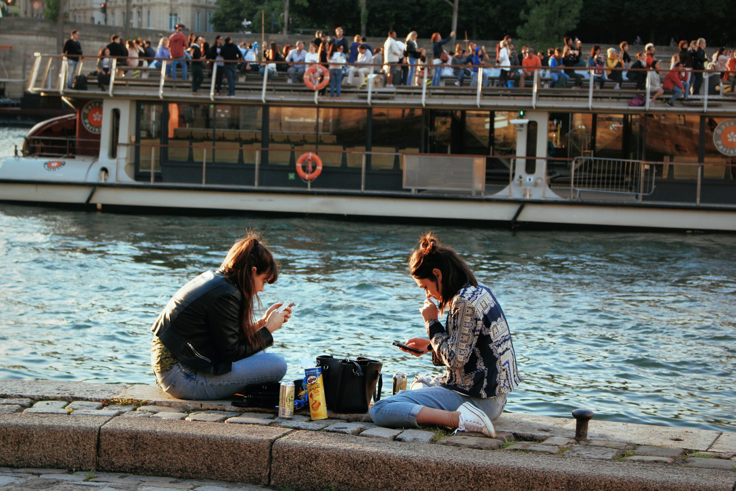 Two women having eating on the banks of the seine with a ferry in the background