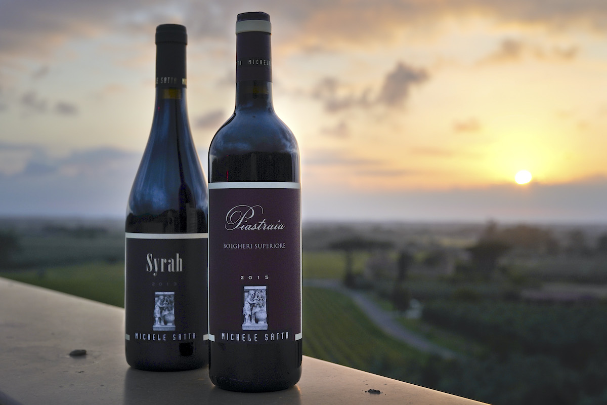 Two bottles of wine with the vineyard at sunset in the background