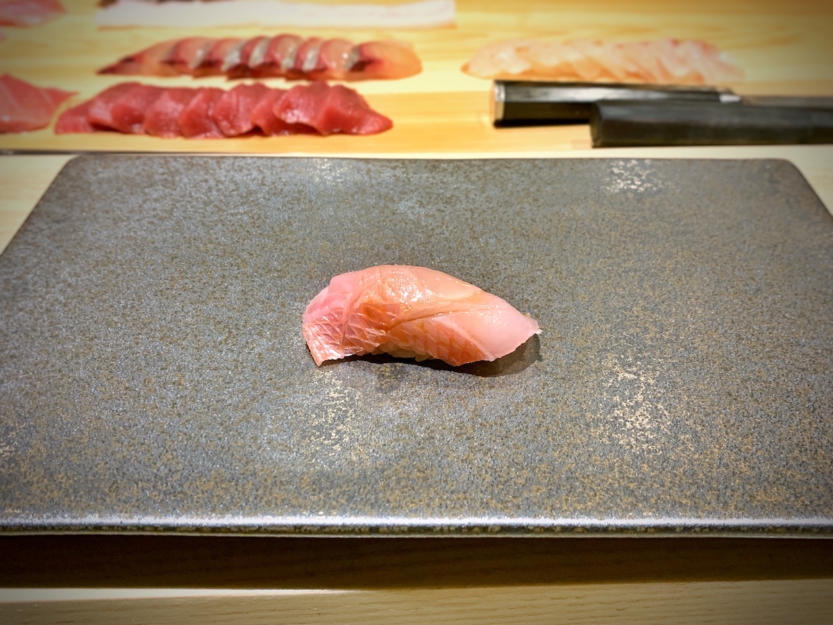 Small piece of pink sushi on a gray square plate.