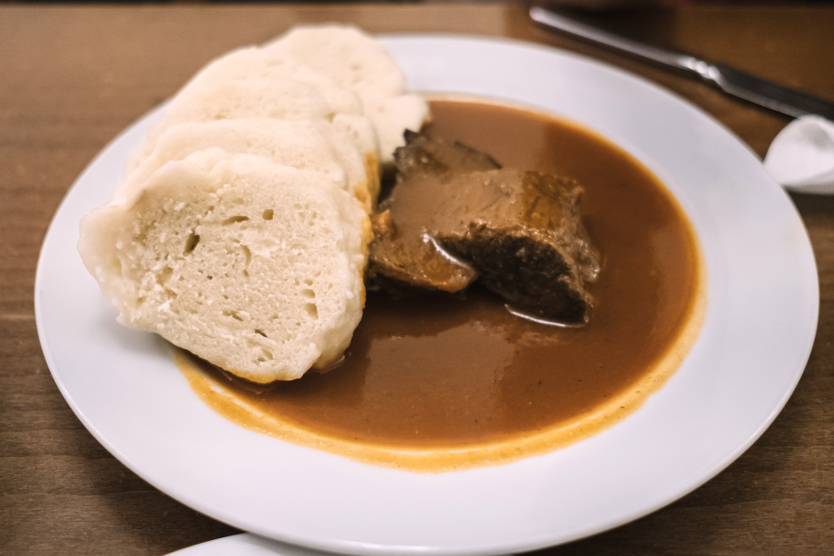 Meat in a brown sauce with several bread dumplings beside it on the same plate.