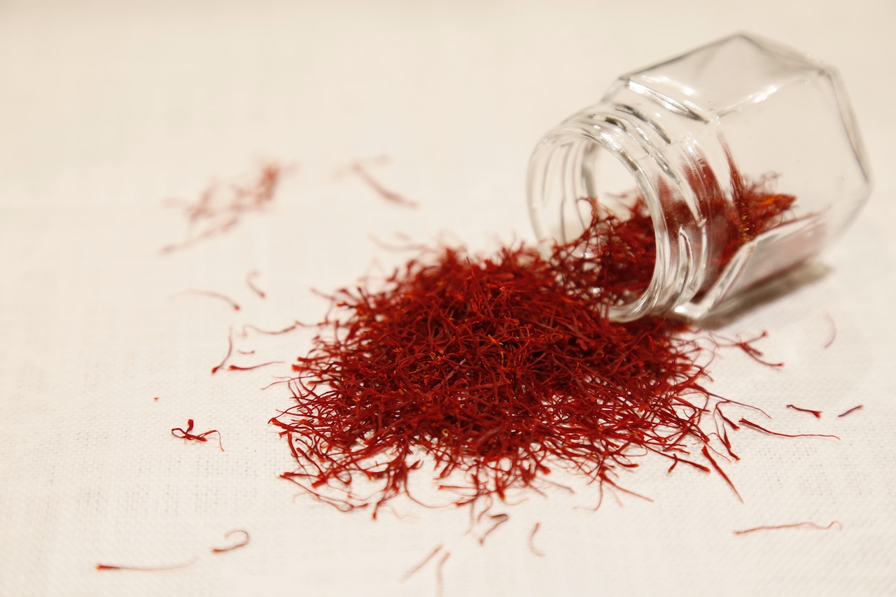 Strands of red saffron spice spilling from a glass container