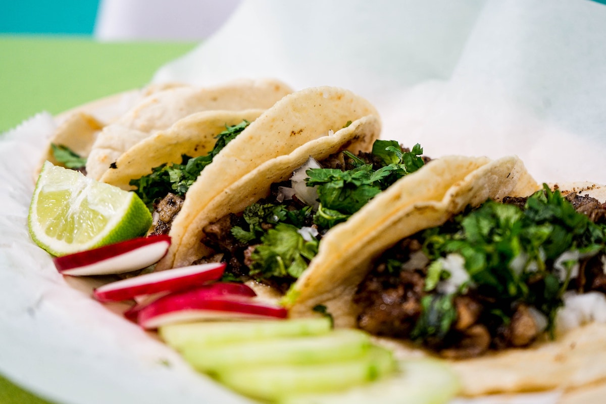 Soft tacos filled with meat, onions, and cilantro and garnished with cucumber, radish, and lime.