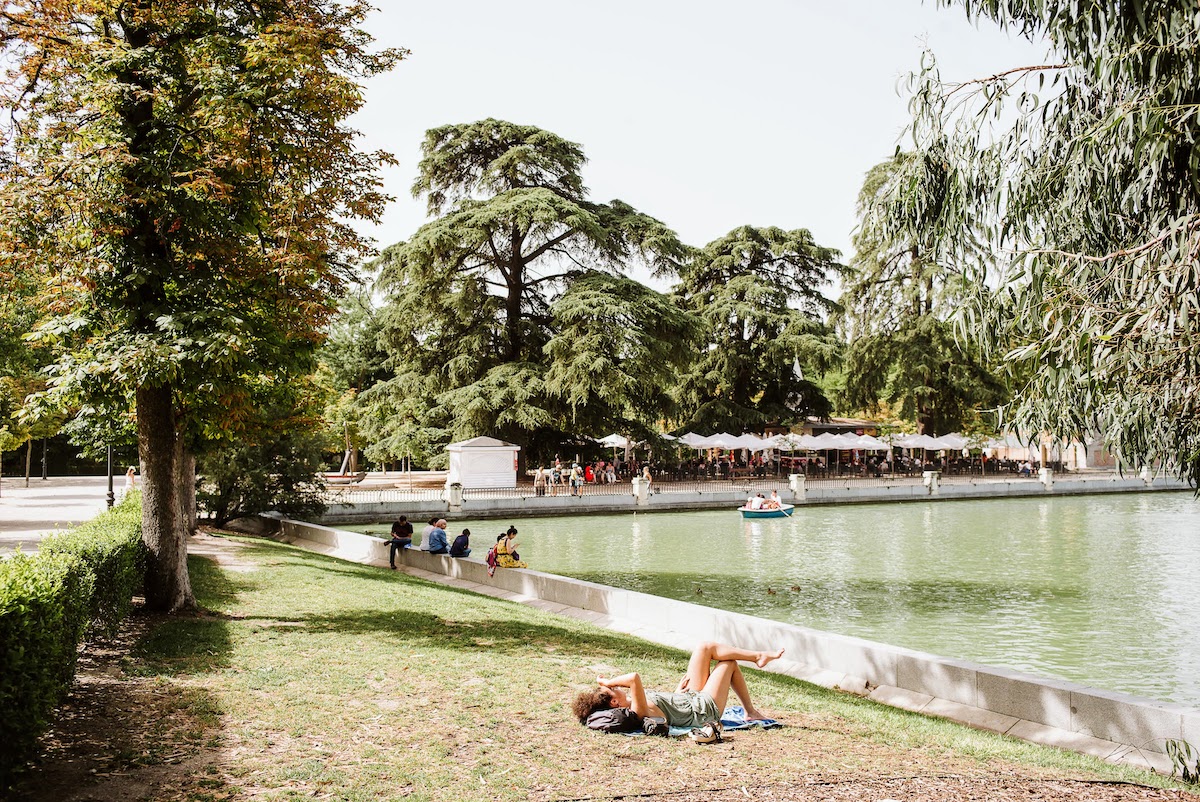 A person lying in the grass next to a body of water to tan in the sunshine.