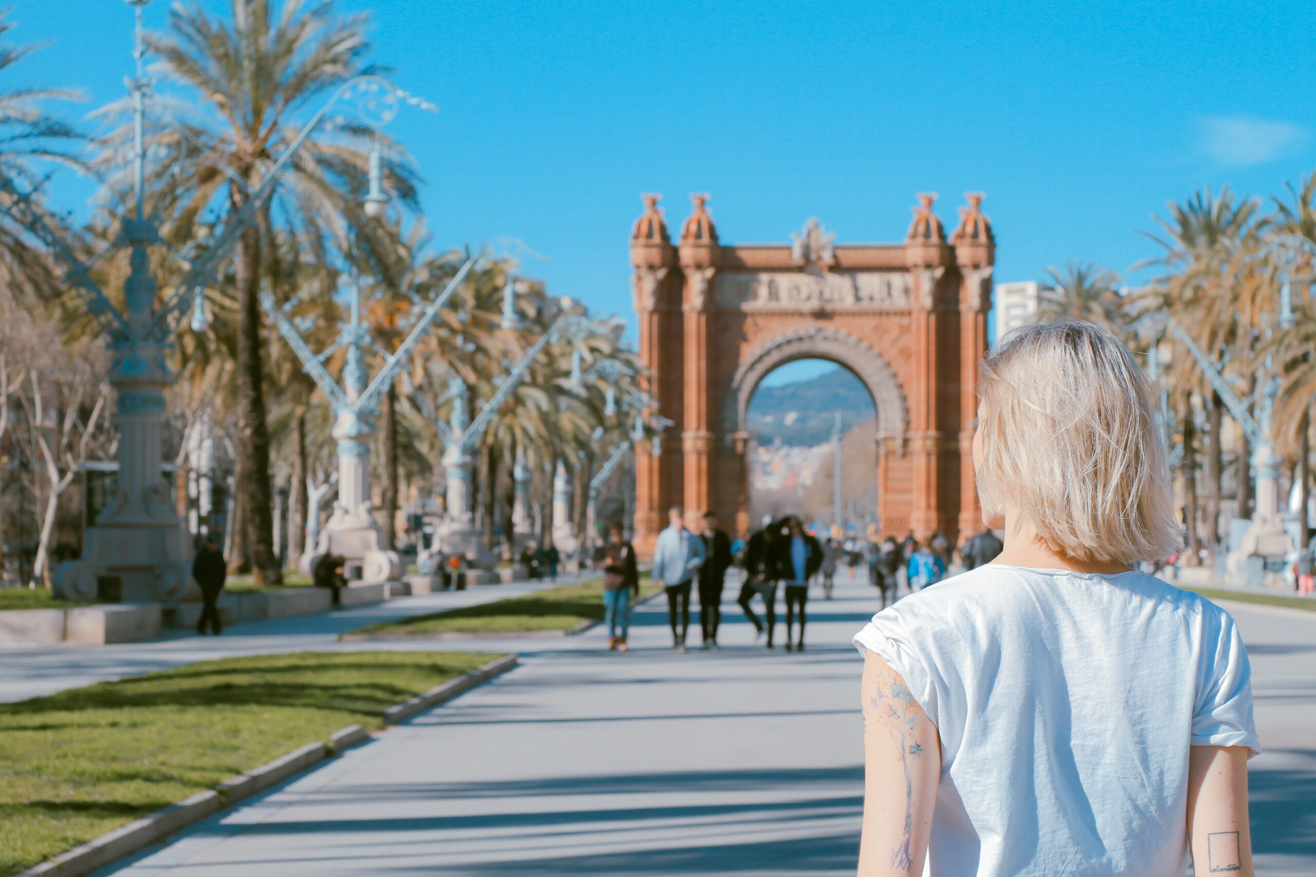 A blonde solo traveller is standing close to the Arco de Triunfo de Barcelona                                                                                                             