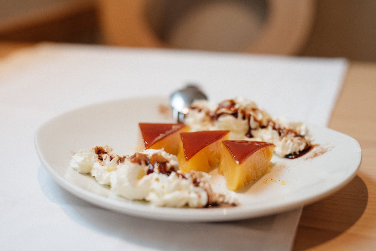 Three triangle-shaped pieces of tocino de cielo, a Spanish dessert, on a plate decorated with whipped cream