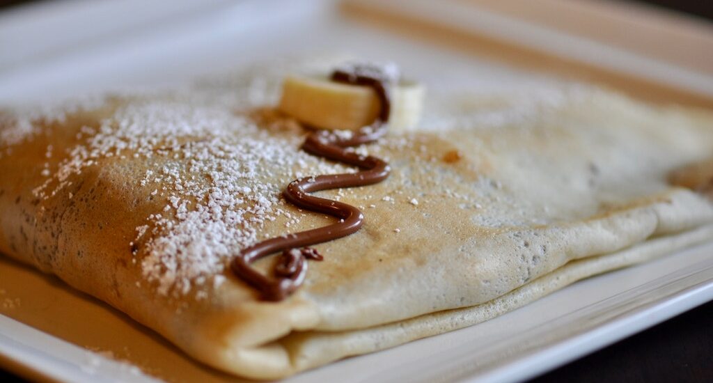 Close-up of folded Parisian crepe drizzled with chocolate, powdered sugar, and banana slices